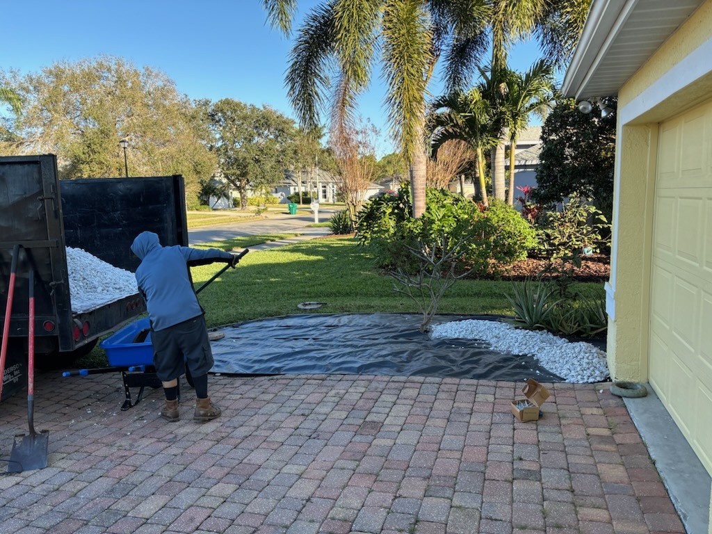 White rock going down over a driveway tarp beside a finished bed